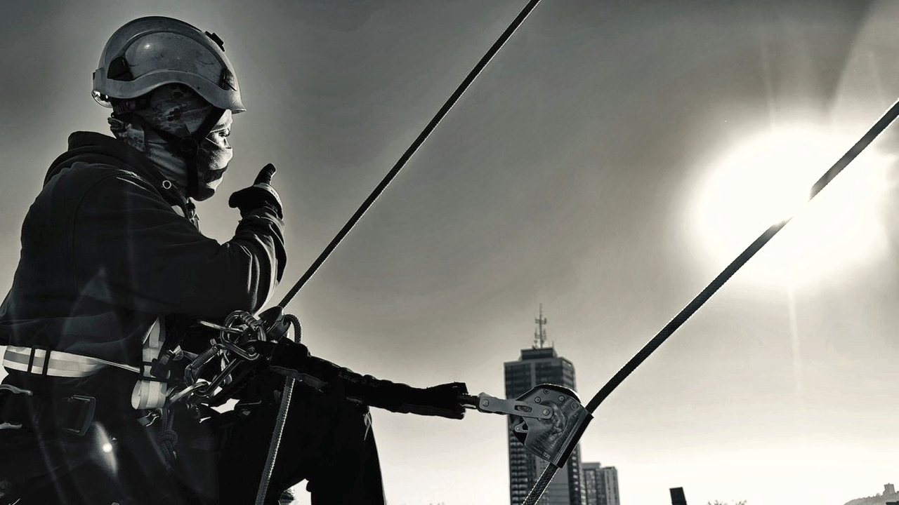 Safe Point rope access technician on a rooftop edge, clipped to a lifeline with a rope grab above a city skyline